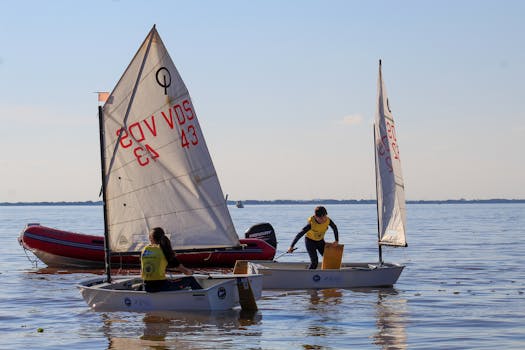 Children sailing small boats on a calm sea under a clear sky, enjoying watersports.
